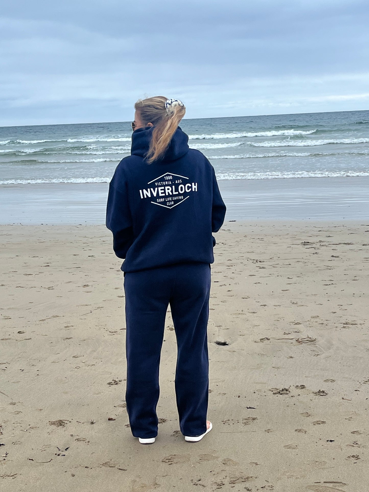 Person wearing a navy hoodie with 'Inverloch' branding on a beach.