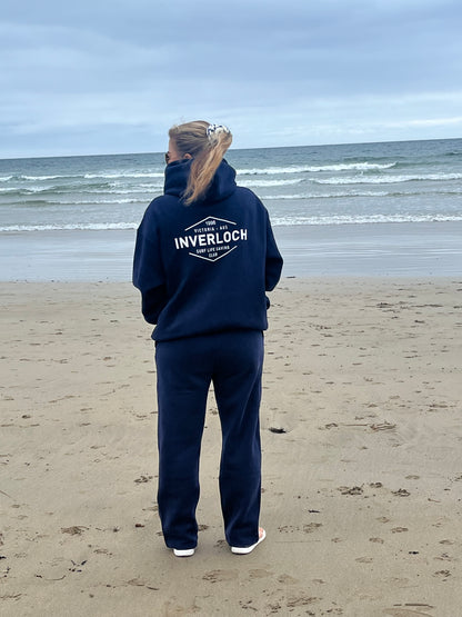 Person wearing a navy hoodie with 'Inverloch' branding on a beach.