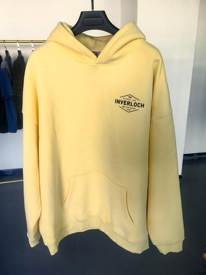 Yellow hoodie with 'INVERLOCH' logo on a hanger against a white wall.